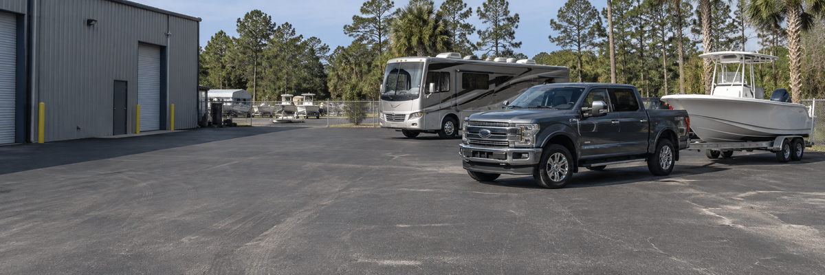Pickup with boat trailer and a touring RV in a clean outdoor service yard in daylight